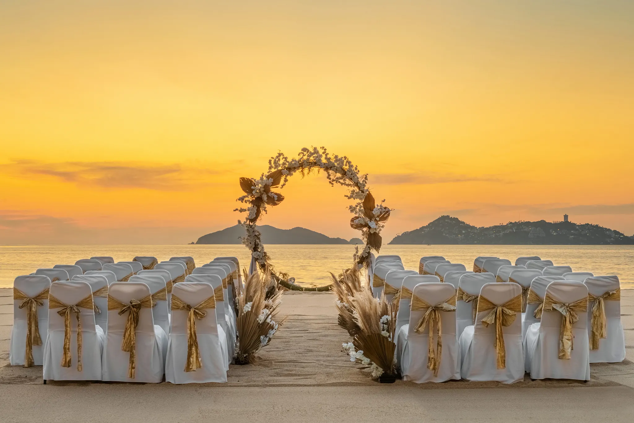 Beach wedding ceremony setup with floral arch at sunset at Dreams Acapulco Resort & Spa
