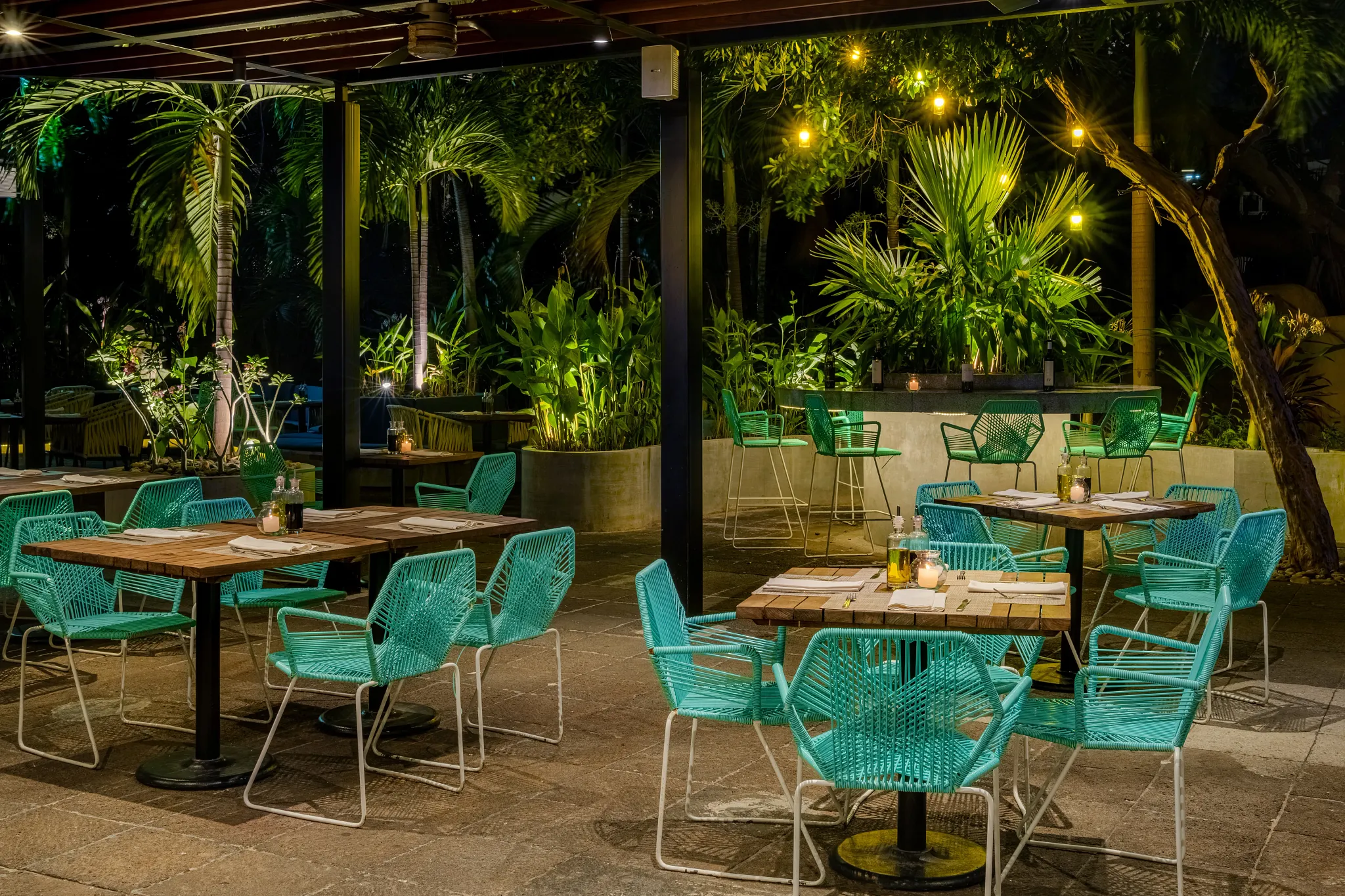 La Trattoria Italian Restaurant at Dreams Acapulco Resort & Spa featuring an outdoor garden terrace with rustic wooden tables and ambient evening lighting.