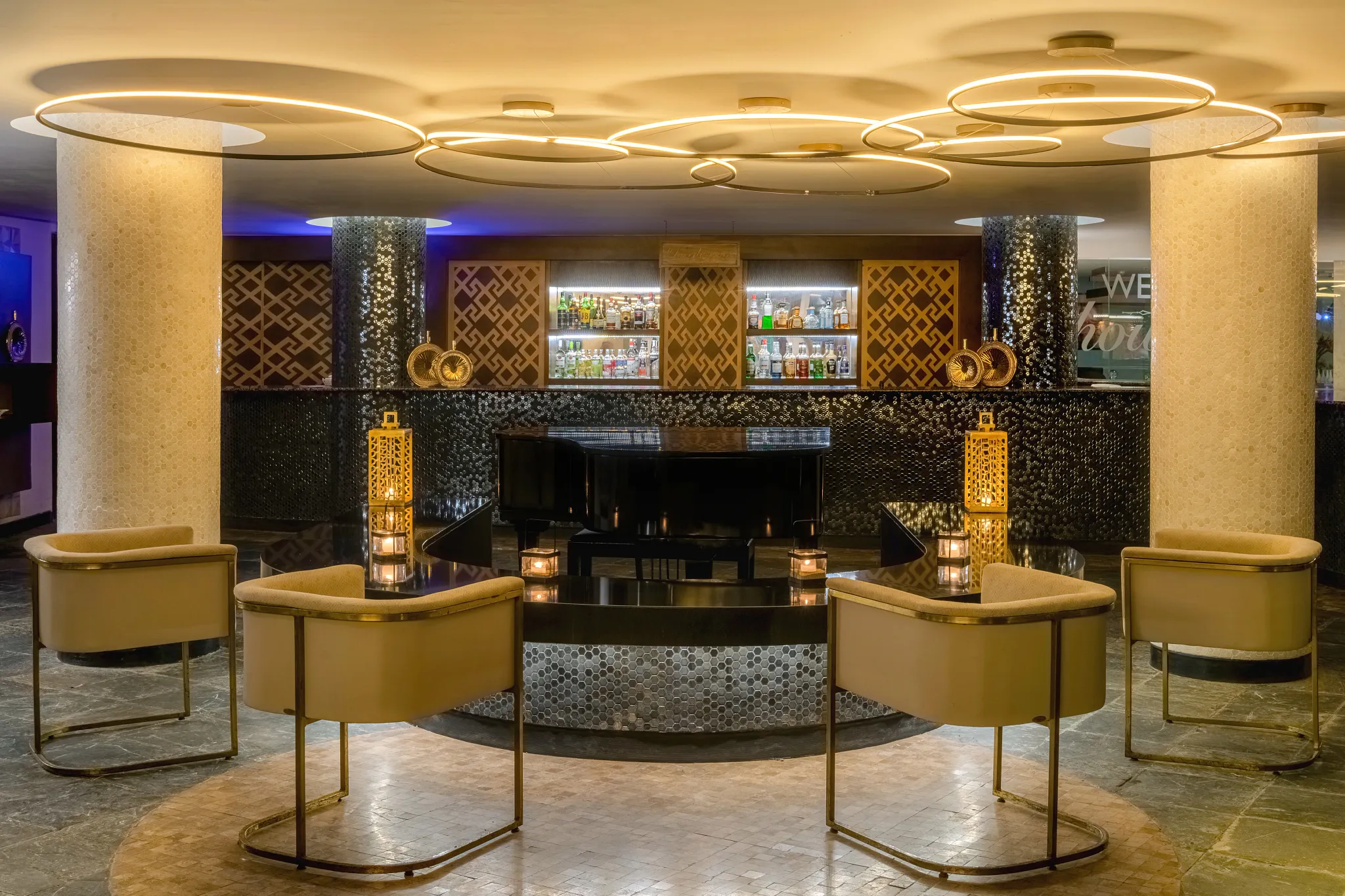 Rendezvous Lobby Bar at Dreams Acapulco Resort & Spa featuring elegant lounge seating, a grand piano, and a stylish illuminated bar backdrop.